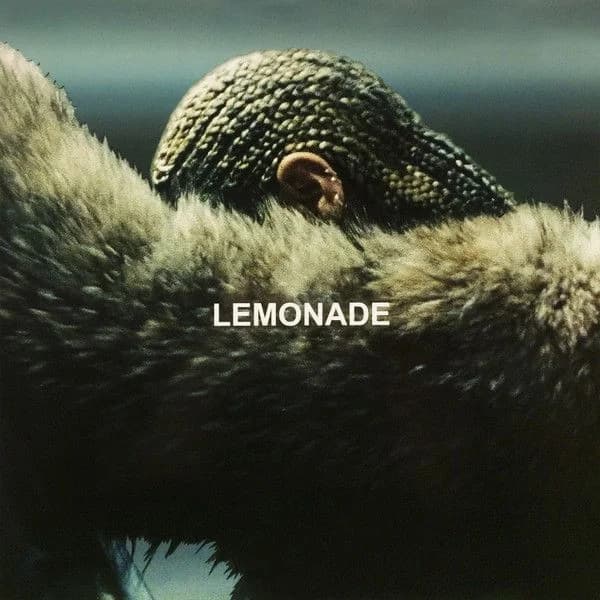 Beyonce wearing cornrows and a brown fur coat, leaning against a car with her arm obscuring her face; the title "Lemonade" is overlaid in white text in the center of the image.